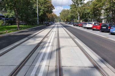 Tram rail track in street with parked cars and cars driving by and trees