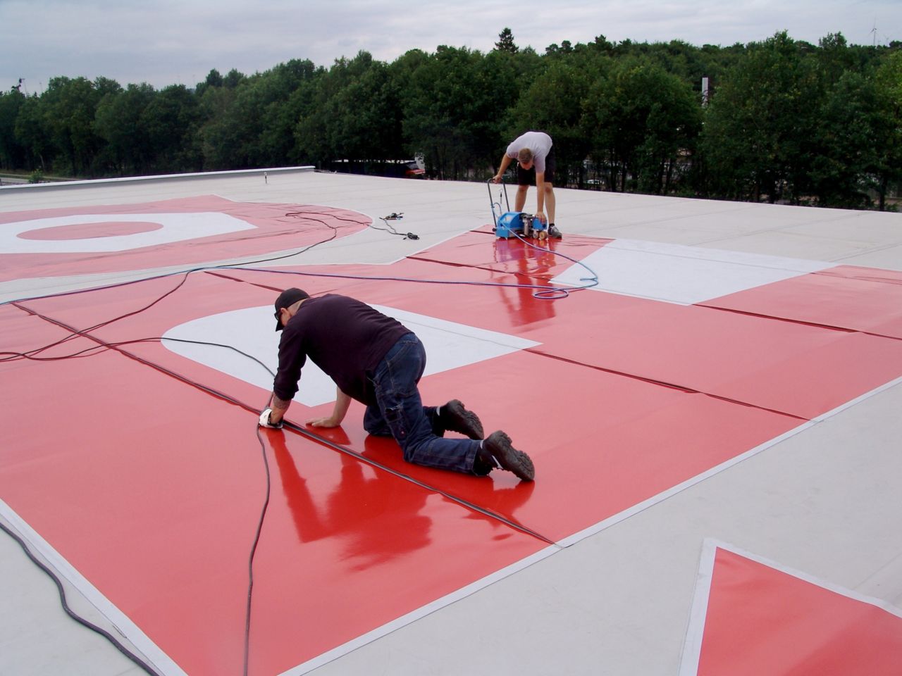 Men welding red colored Sika roof graphic onto roof