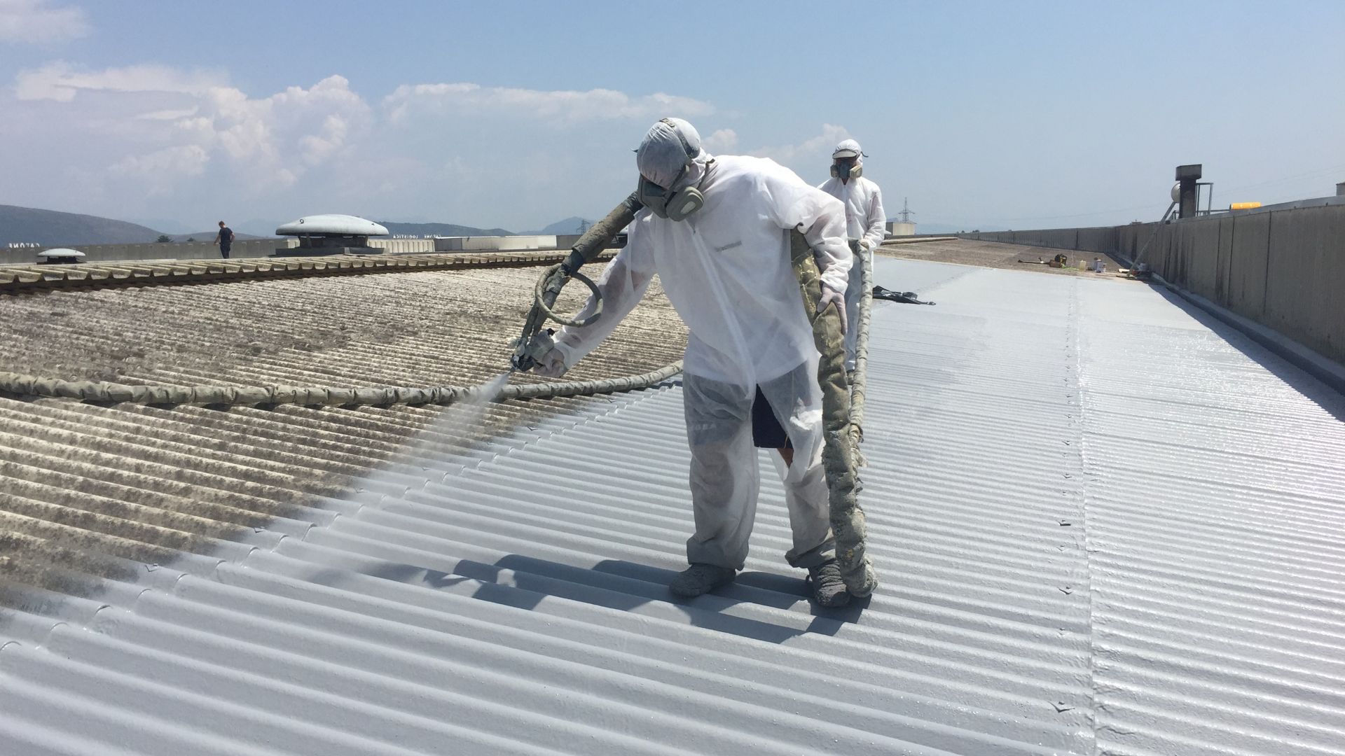 Applicators applying liquid applied membrane to corrugated metal roof in protective clothing