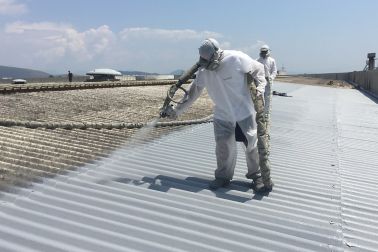 Applicators applying liquid applied membrane to corrugated metal roof in protective clothing