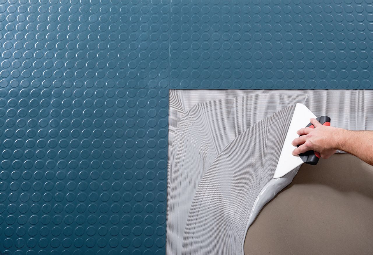 Blue rubber tile floor being bonded with adhesive applied by hand trowel, view from above