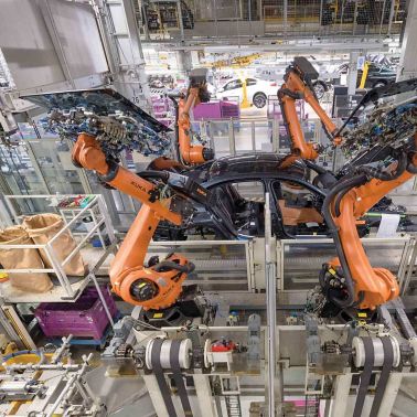 Body in white on assembly line while robots place glass on vehicle body with Sika Assembly Adhesives