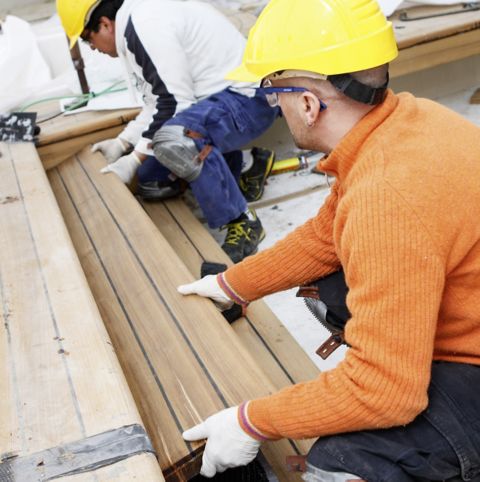 two men's applying adhesive to caulk the deck