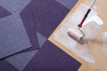 Purple carpet tile floor being bonded with adhesive applied by roller brush, view from above