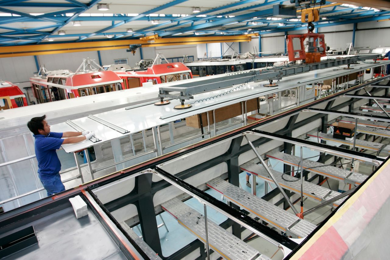 Worker and machines assembling trains in manufacturing factory 