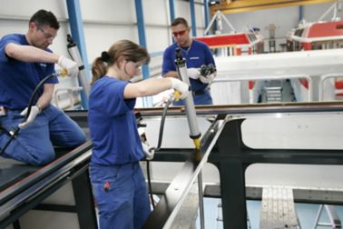 people applying adhesive with a manual gun to a rail roof top