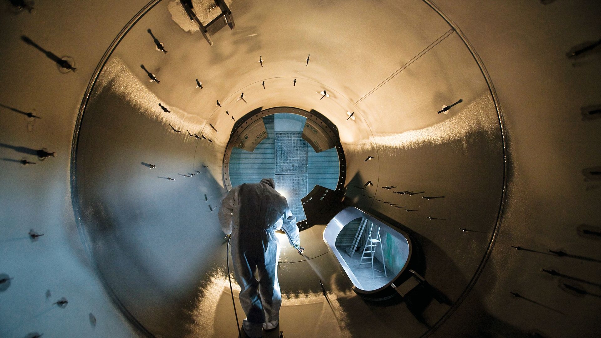 Man in protective clothing applying white corrosion protection coating to inside of wine turbine steel structure