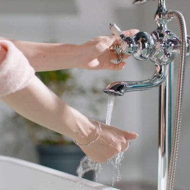 Woman washing hands under tapped water.