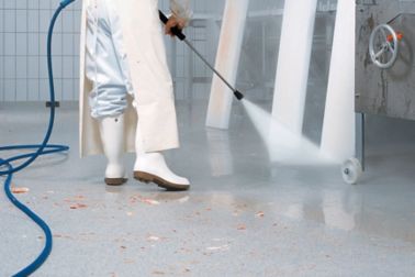 Worker white boots power washing floor with hose in food industry