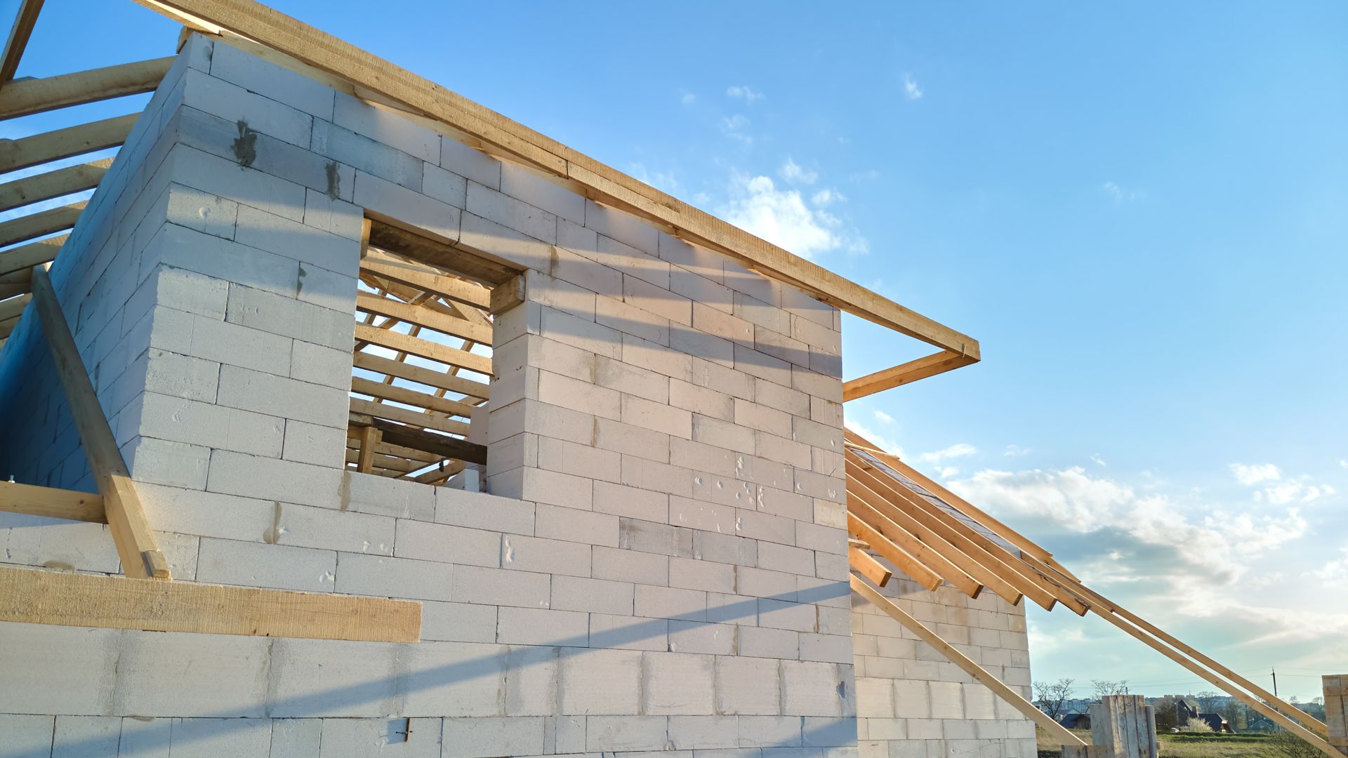 Aerial view of unfinished frame of private house with aerated lightweight concrete walls and wooden roof frame under construction.