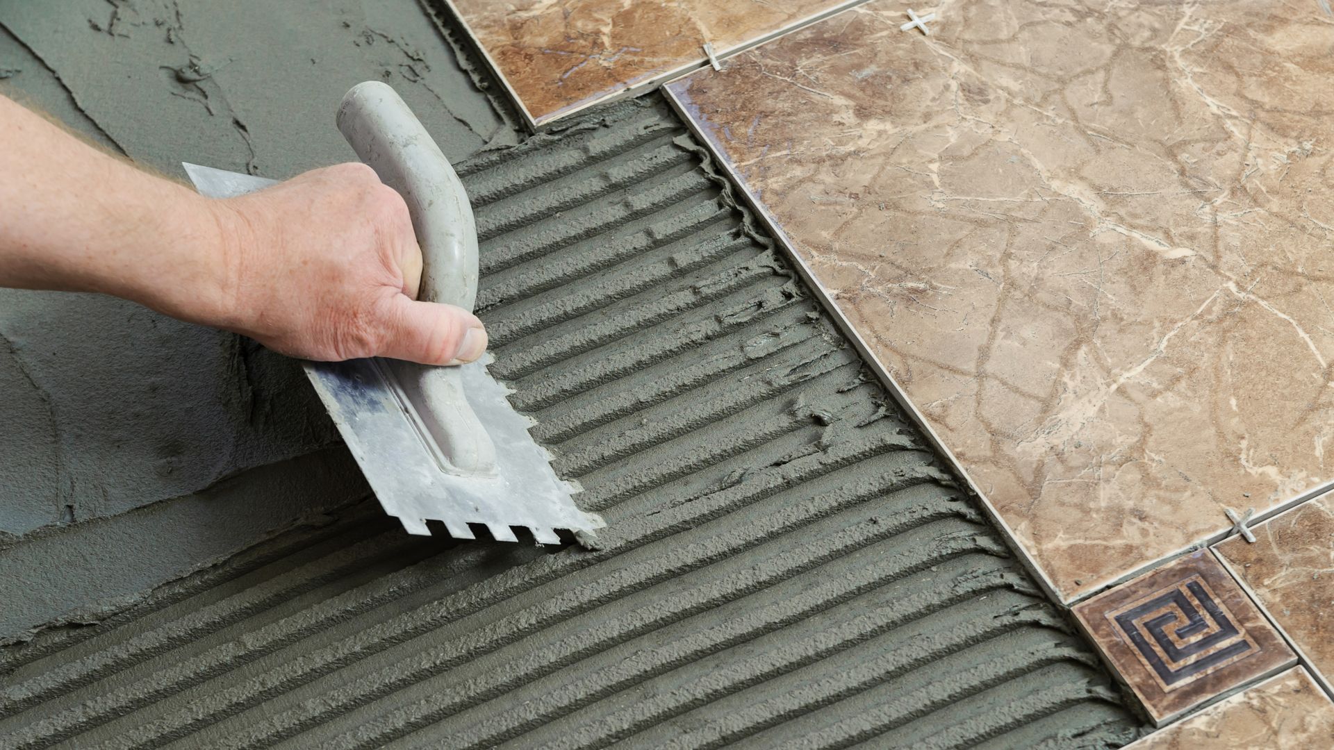 Laying Ceramic Tiles. Troweling adhesive onto a concrete floor in preparation for laying white floor tile.