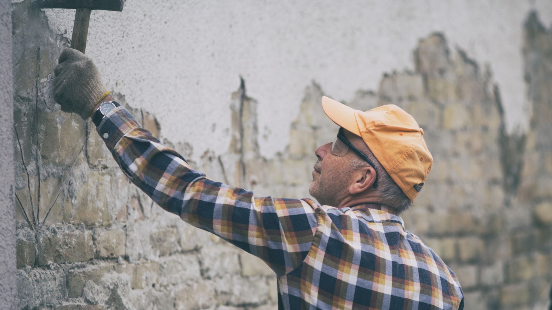 Mature construction worker breaking mortar from old brick wall