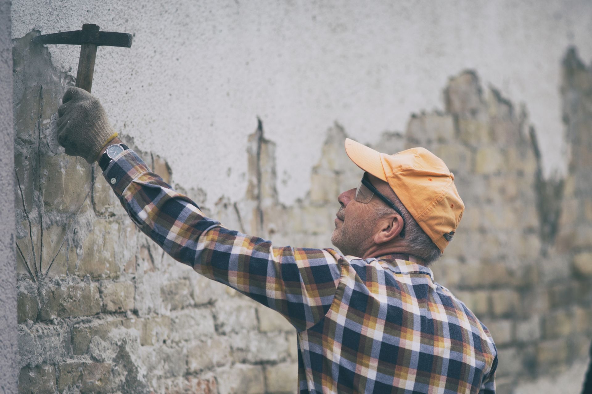 Mature construction worker breaking mortar from old brick wall