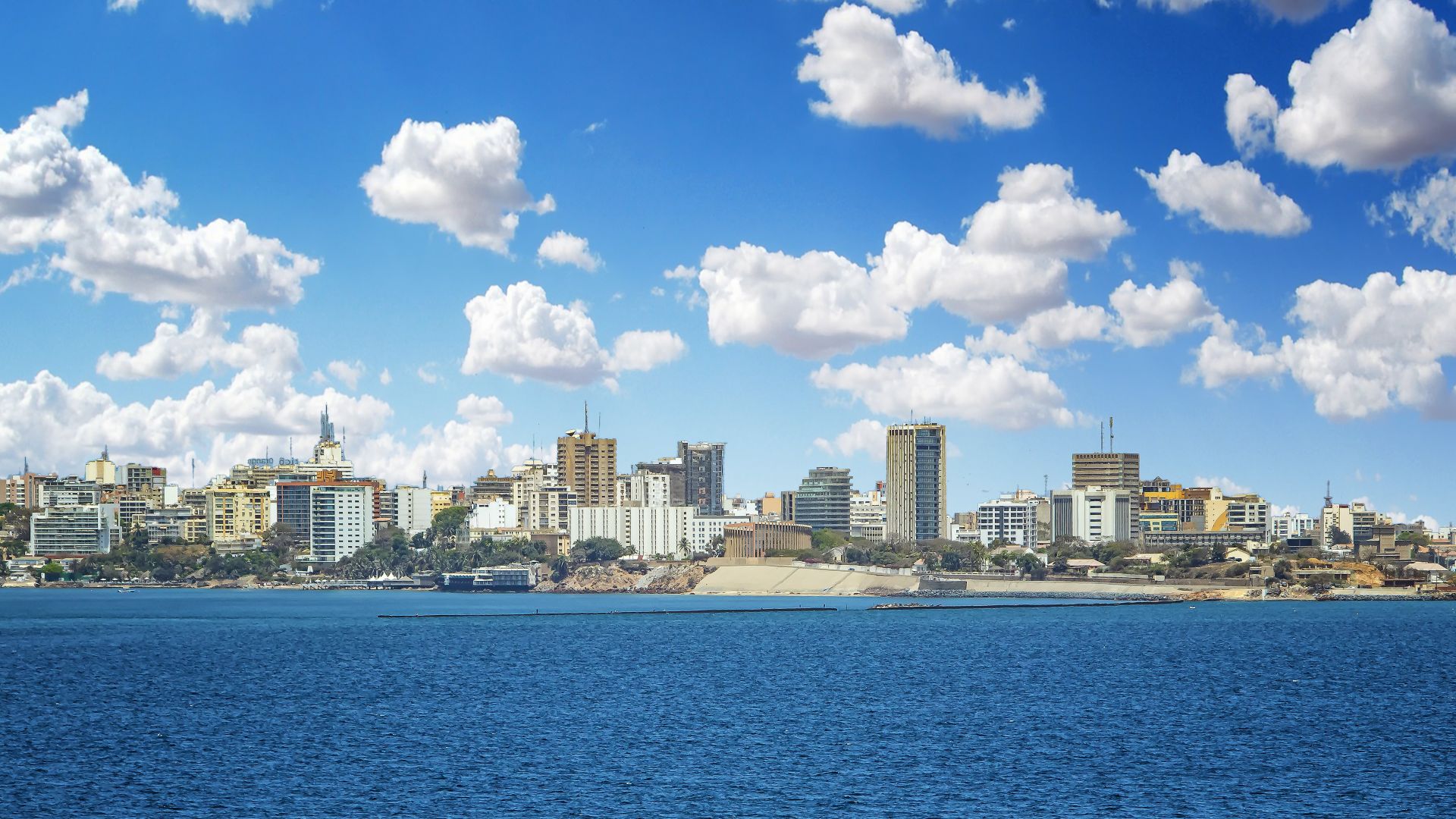 View of the Senegal capital of Dakar, Africa. It is a city panorama taken from a boat. There are large modern buildings and a blue sky with clouds. It's summer.