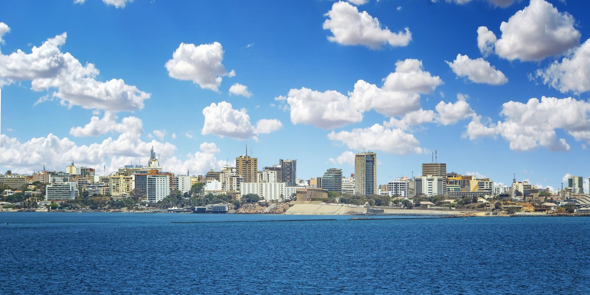 View of the Senegal capital of Dakar, Africa. It is a city panorama taken from a boat. There are large modern buildings and a blue sky with clouds. It's summer.