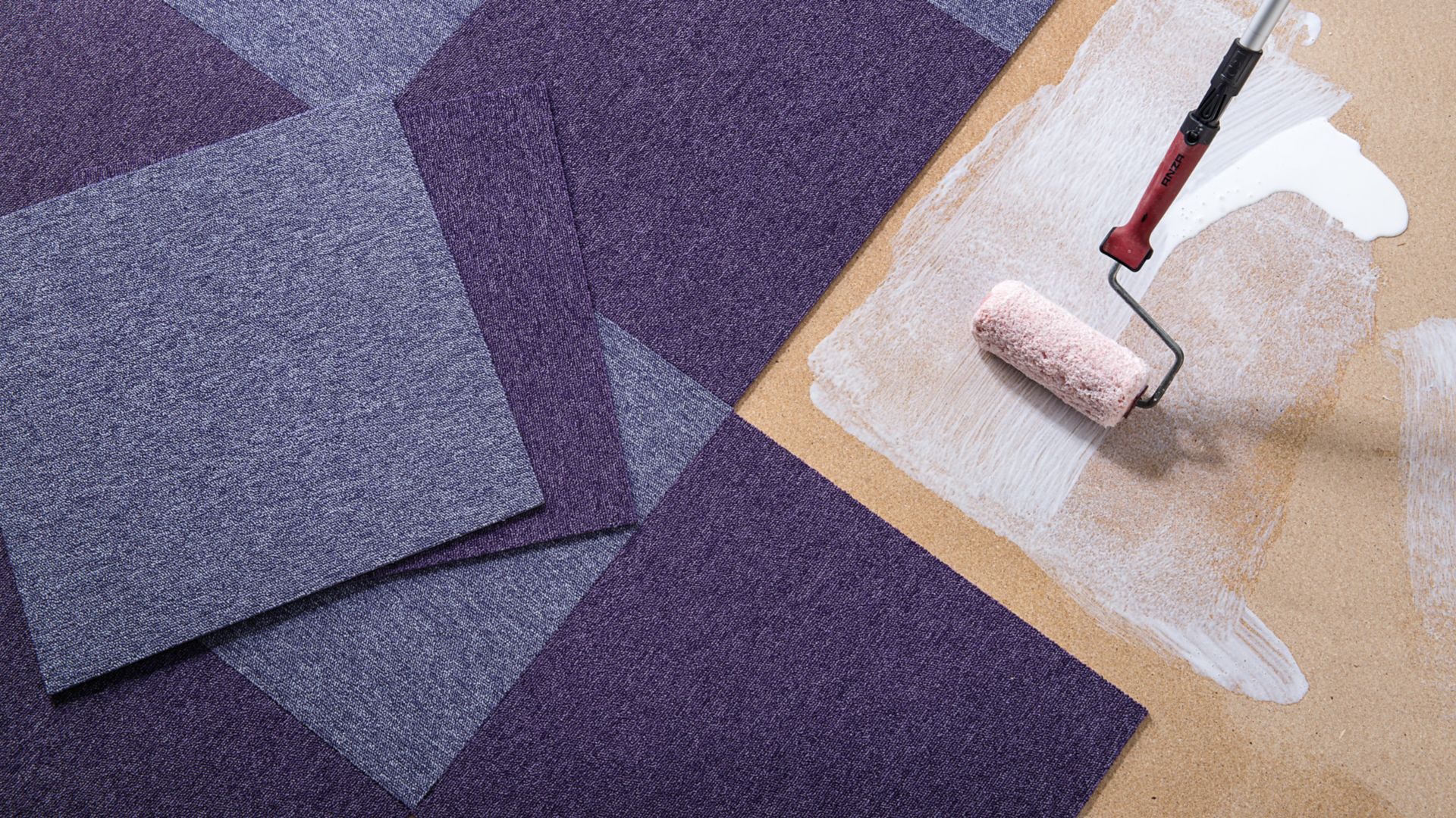 Purple carpet tile floor being bonded with adhesive applied by roller brush, view from above