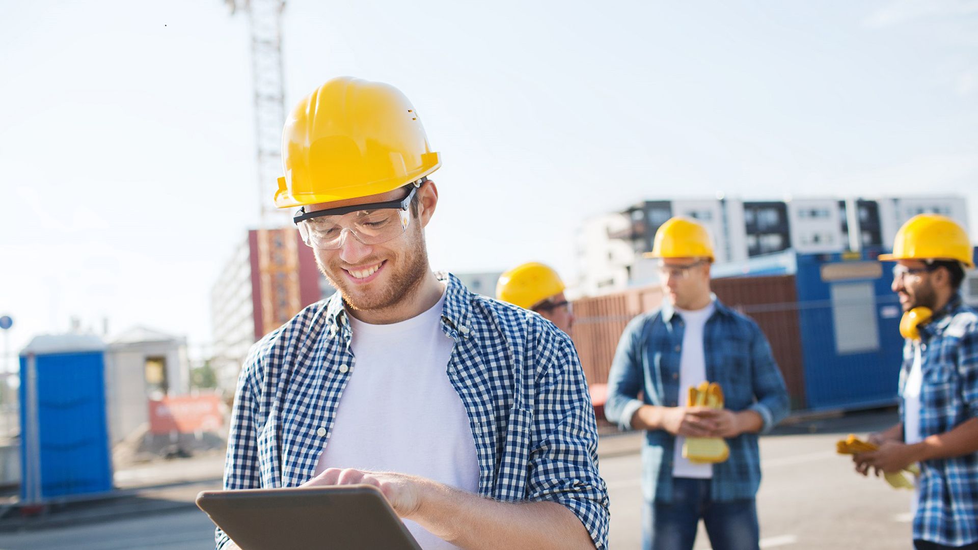 Group of smiling builders men in hardhats with tablet outdoors on construction site