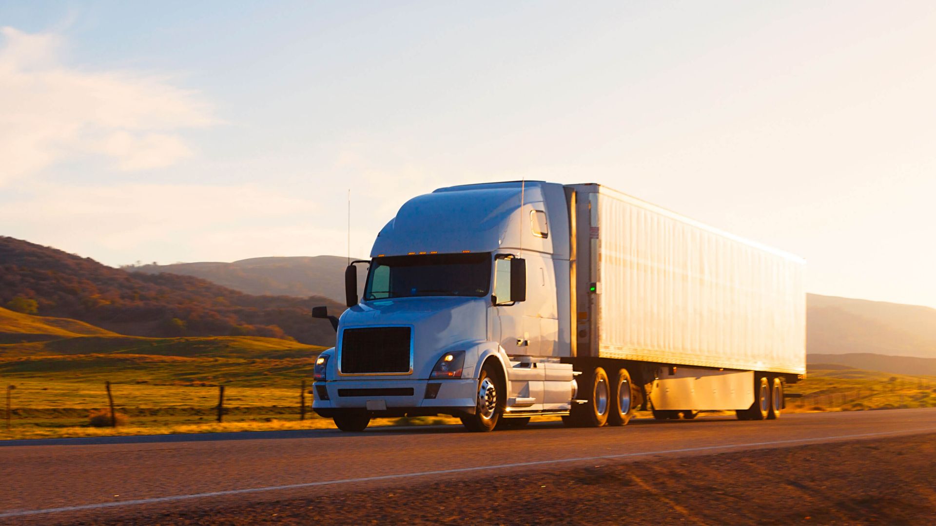 Semi-truck driving on open road at sunrise.