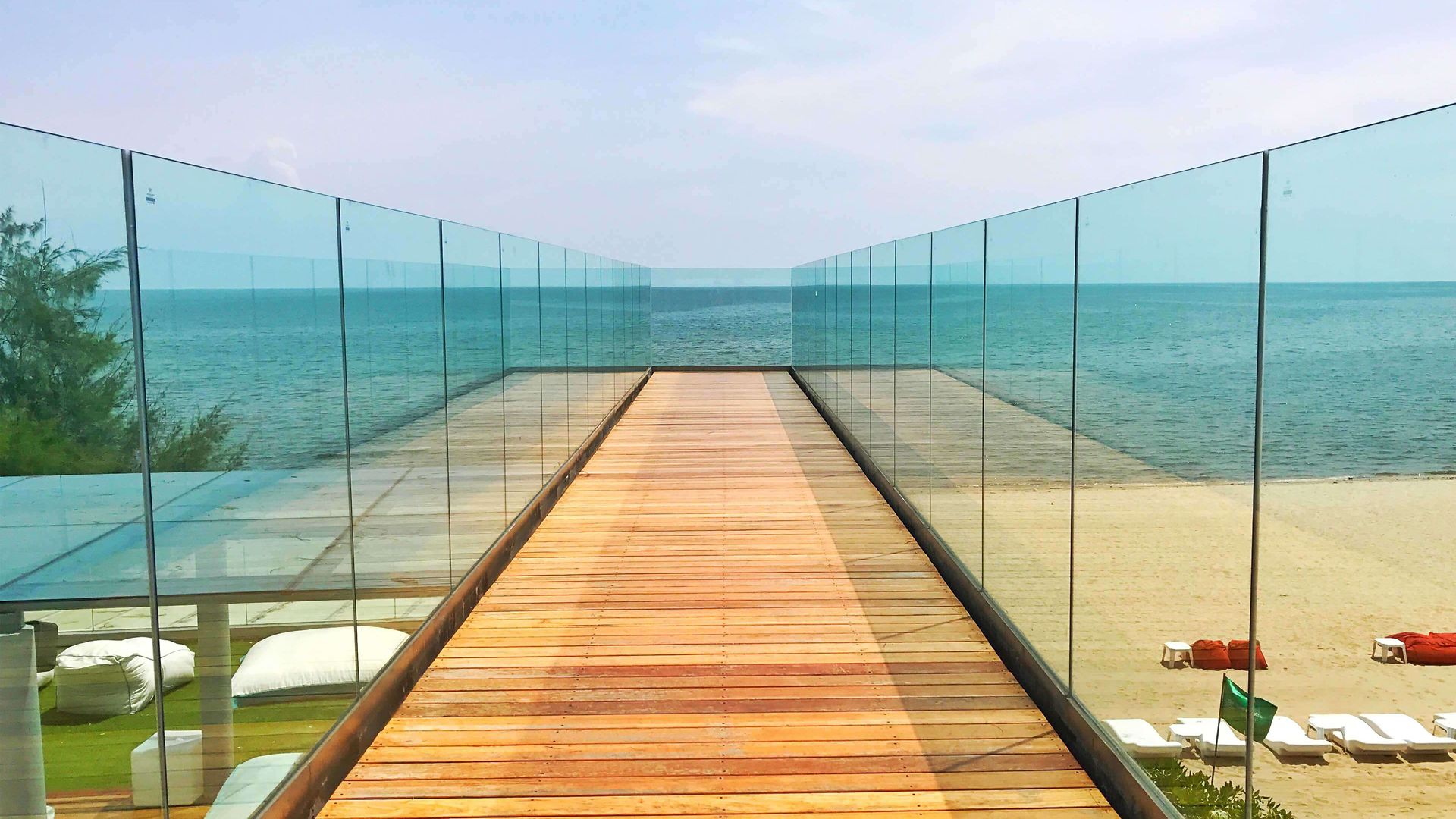 Glass railing on beach boardwalk, glass wall grouting and weather resistant sealing.