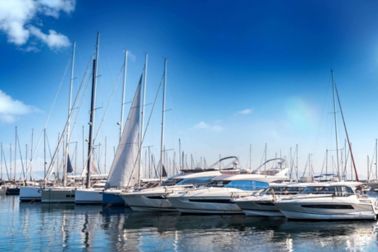 Marina with yachts and sail boats lined up in blue water.  Blue skies with clouds.