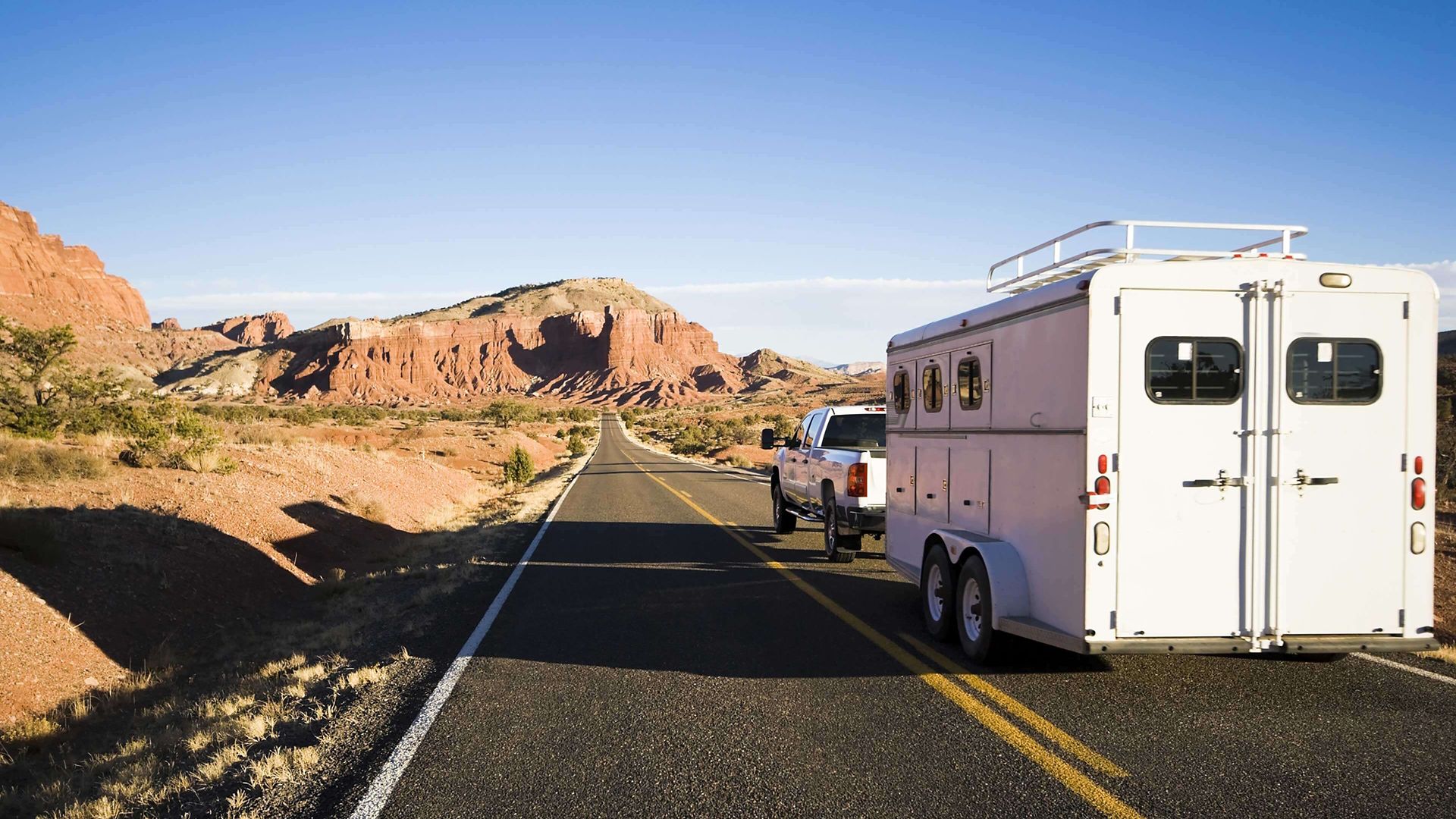 white truck pulling white cargo trailer along highway with mountains; truck pulling horse trailer