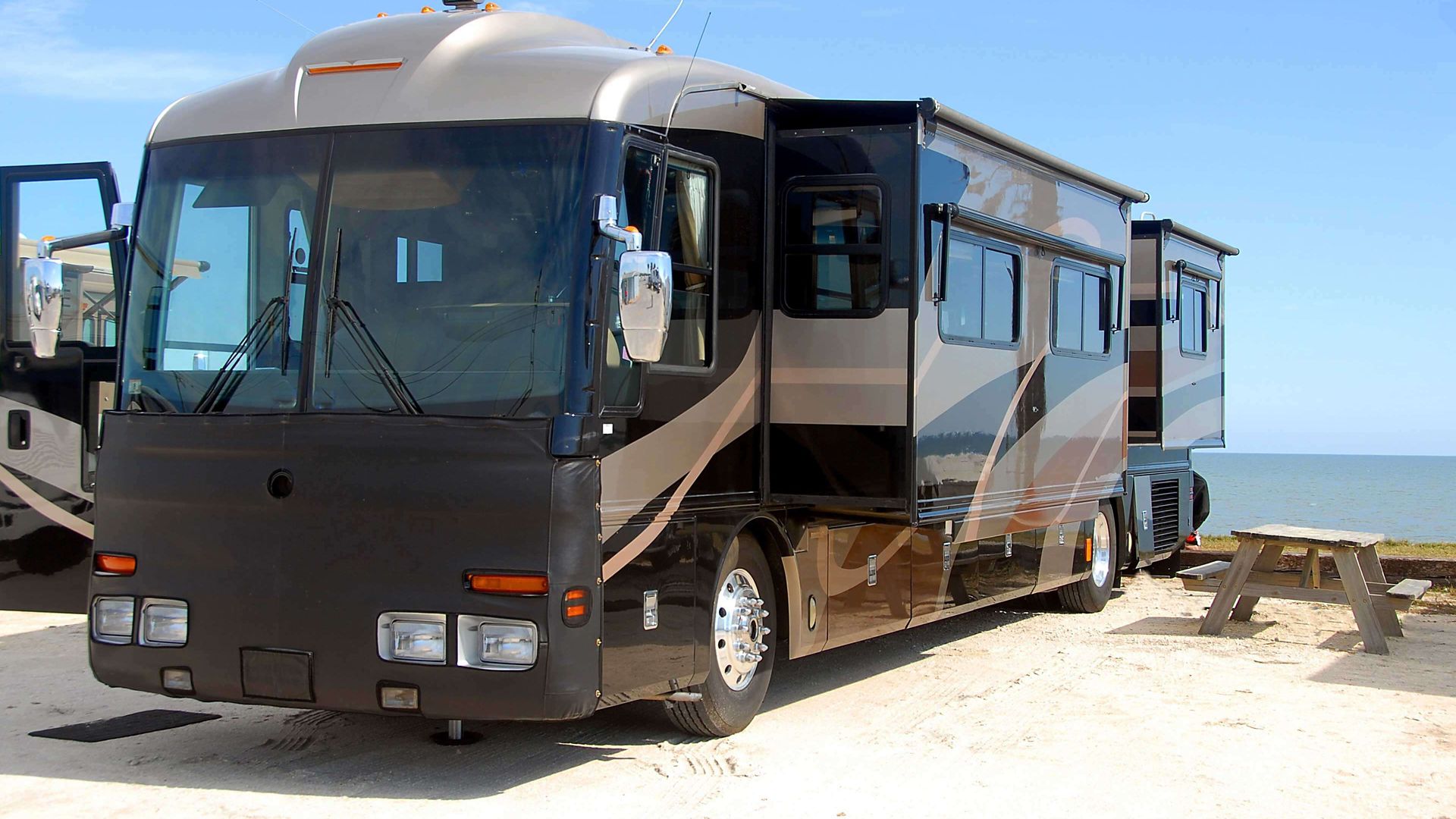 Class A motor home on beach with picnic tables; RV with pop-outs on beach