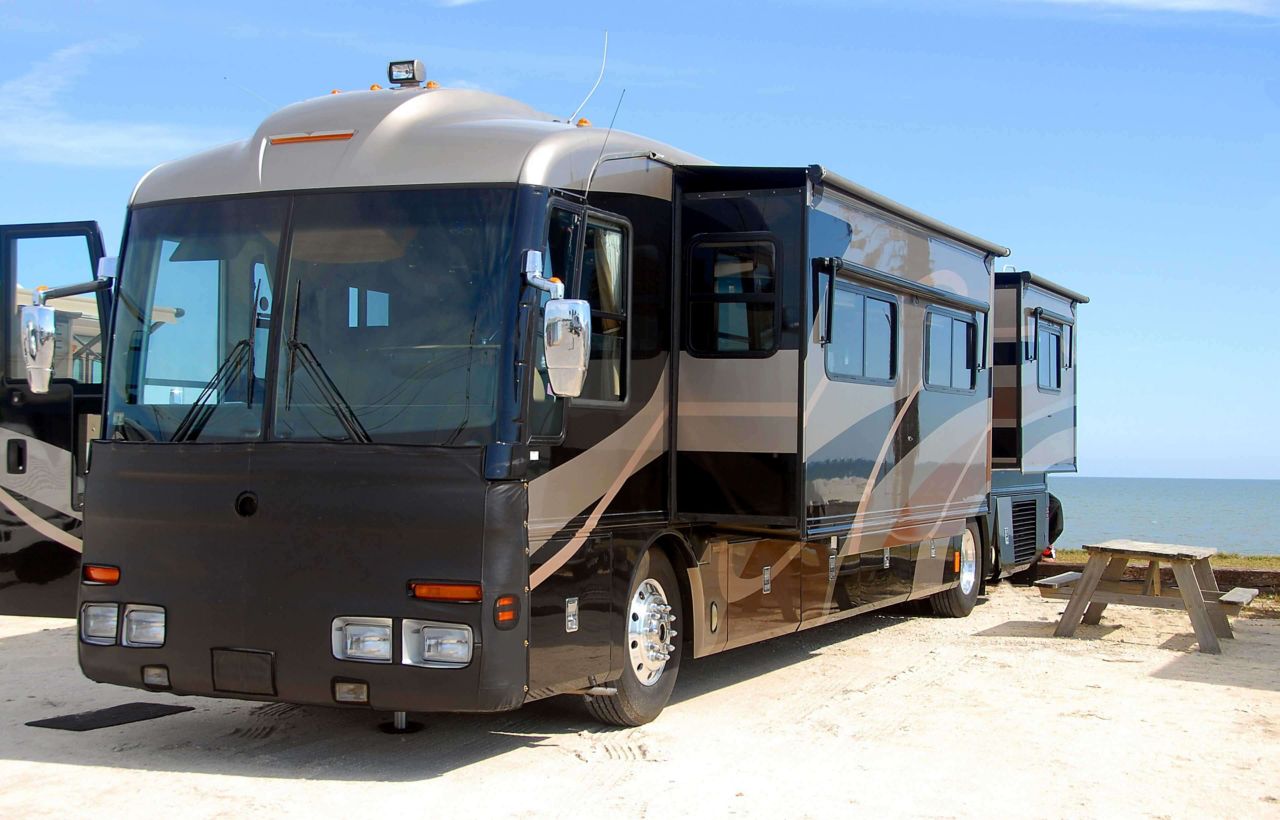 Class A motor home on beach with picnic tables; RV with pop-outs on beach