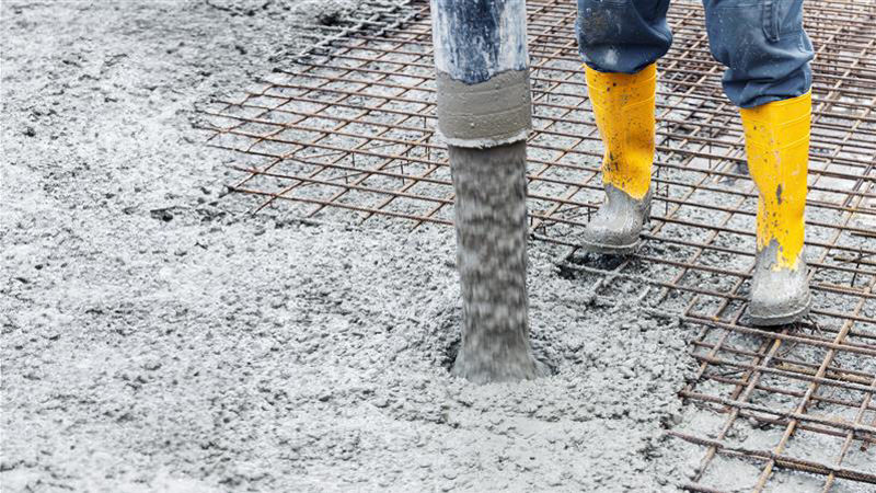 Worker pouring concrete on rebar grid