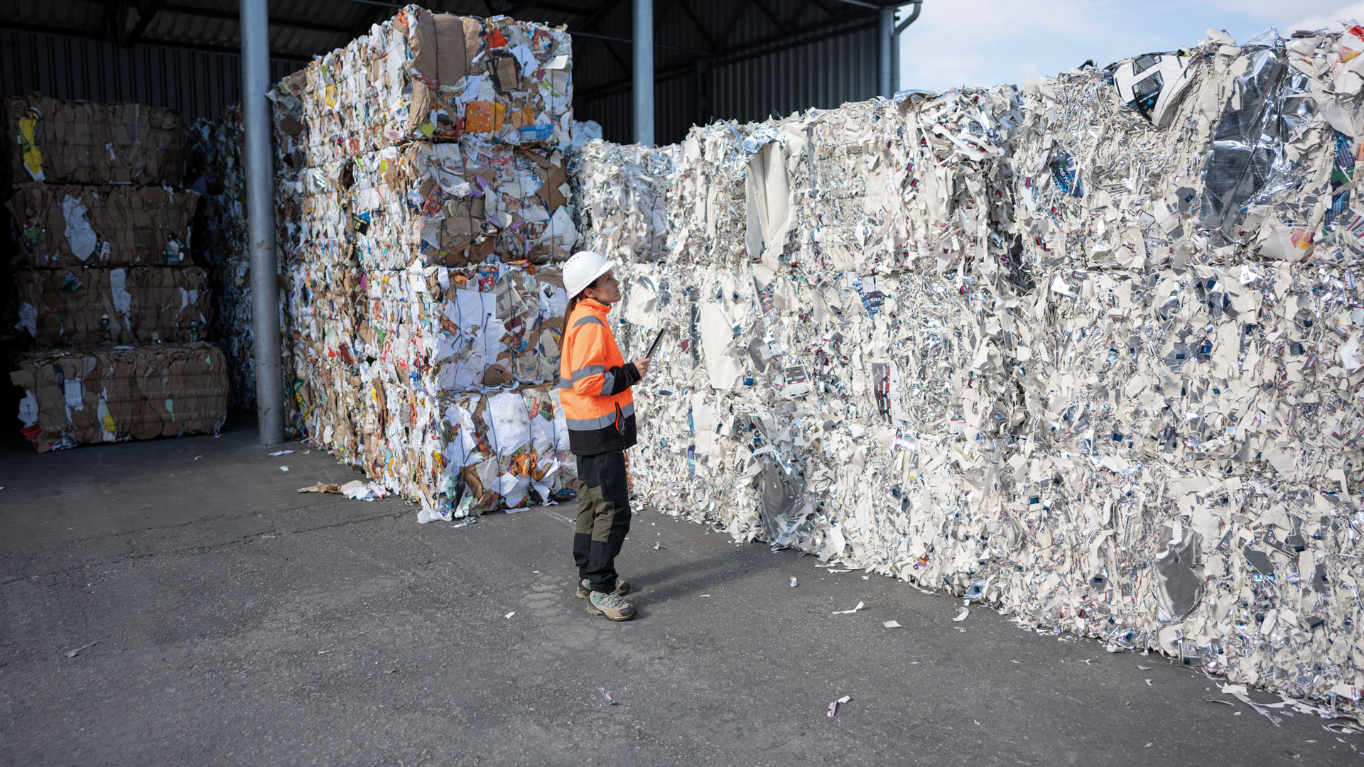 Worker Inspects Large Bales of Recycled Paper Outdoors