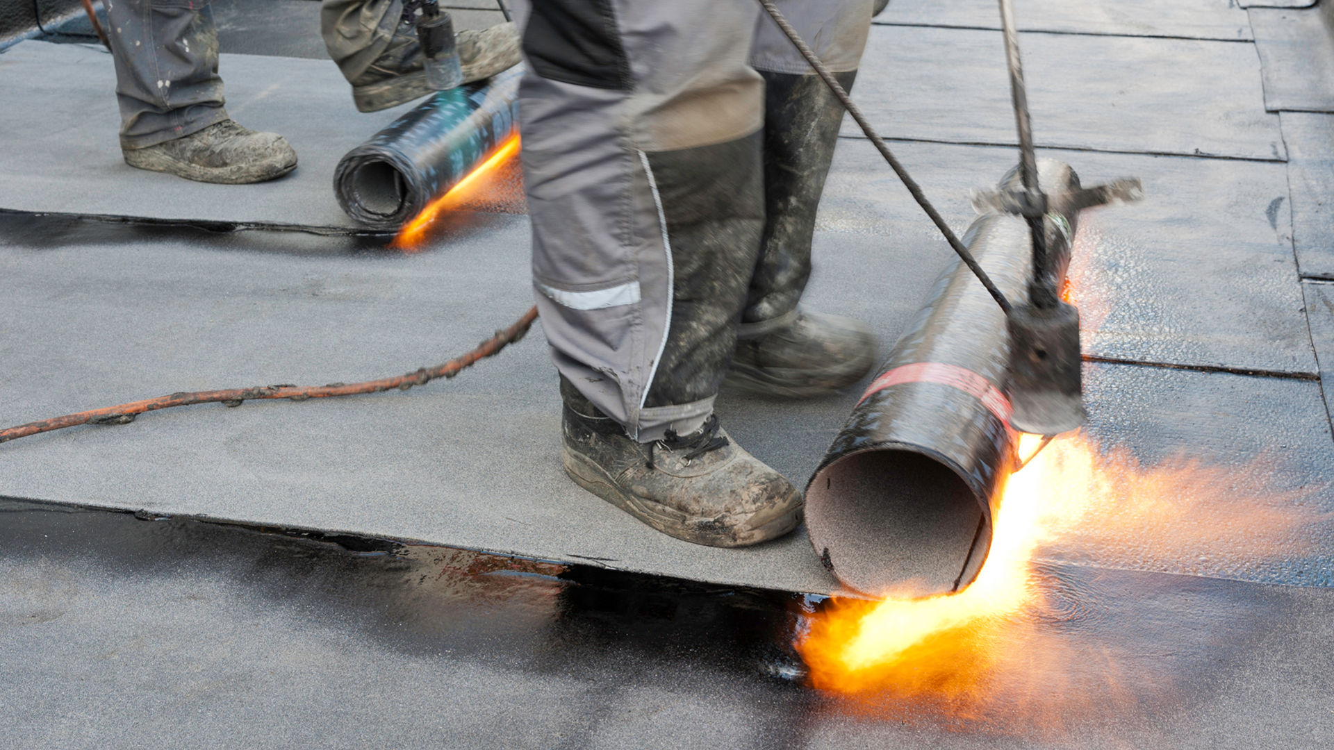 Foot rolling bitumen membrane and applying torch to adhere
