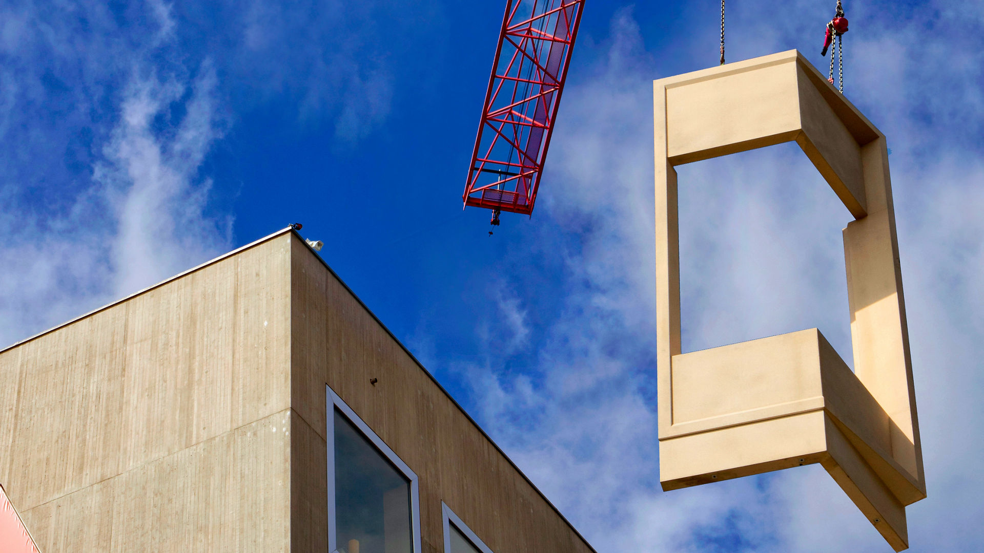 Crane lifts something up. In the background is a large concrete building