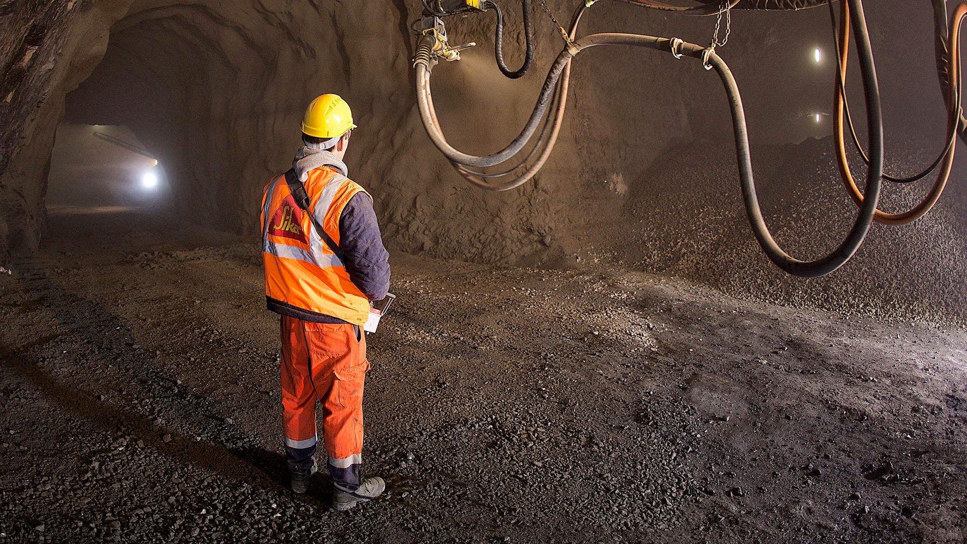 Worker in a mine remote controlling a machine apllying sprayed concrete to the walls of a tunnel