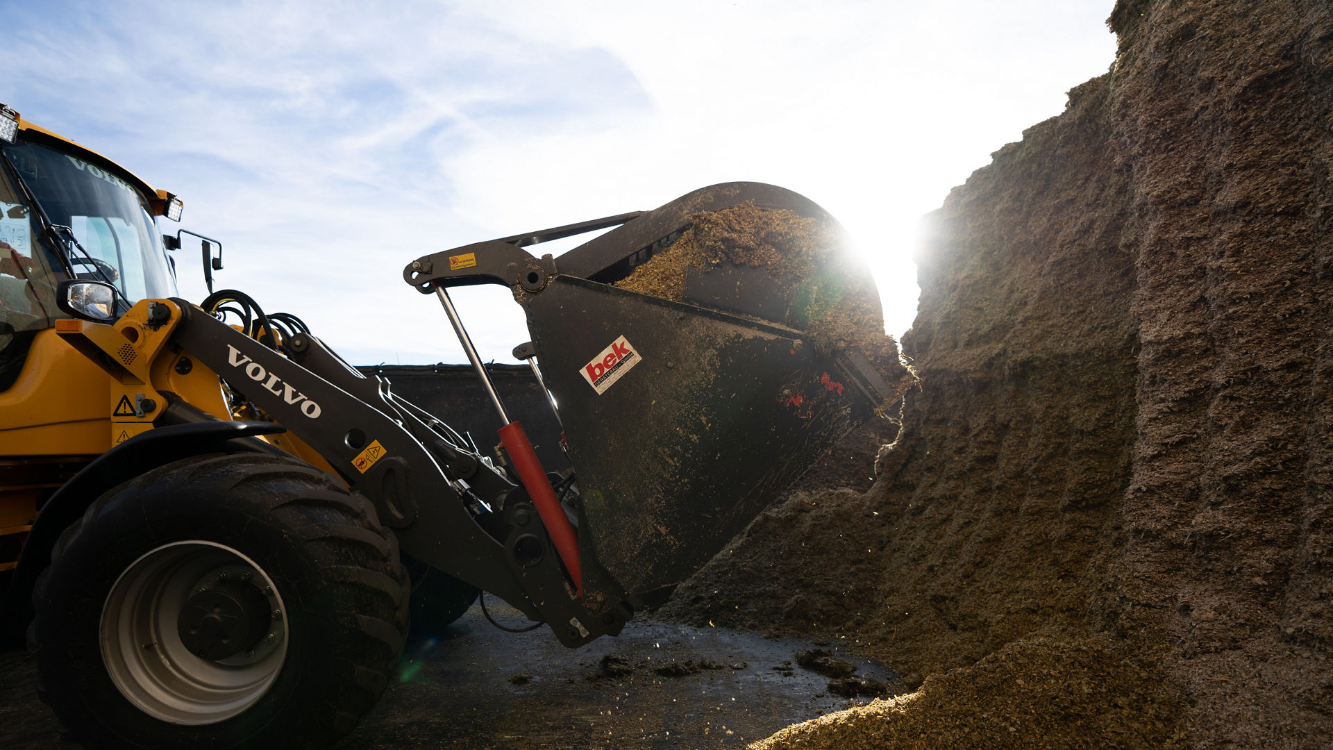 Tractor lifting bale of hay with sun