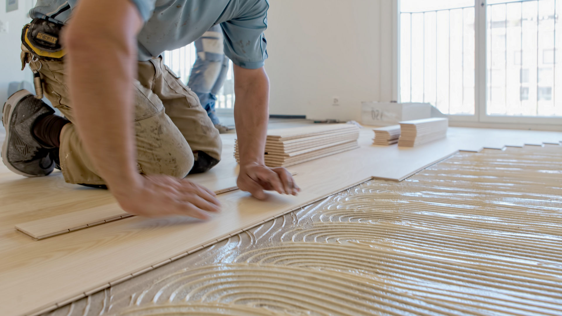 man applying wood panels over wood floor bonding adhesive