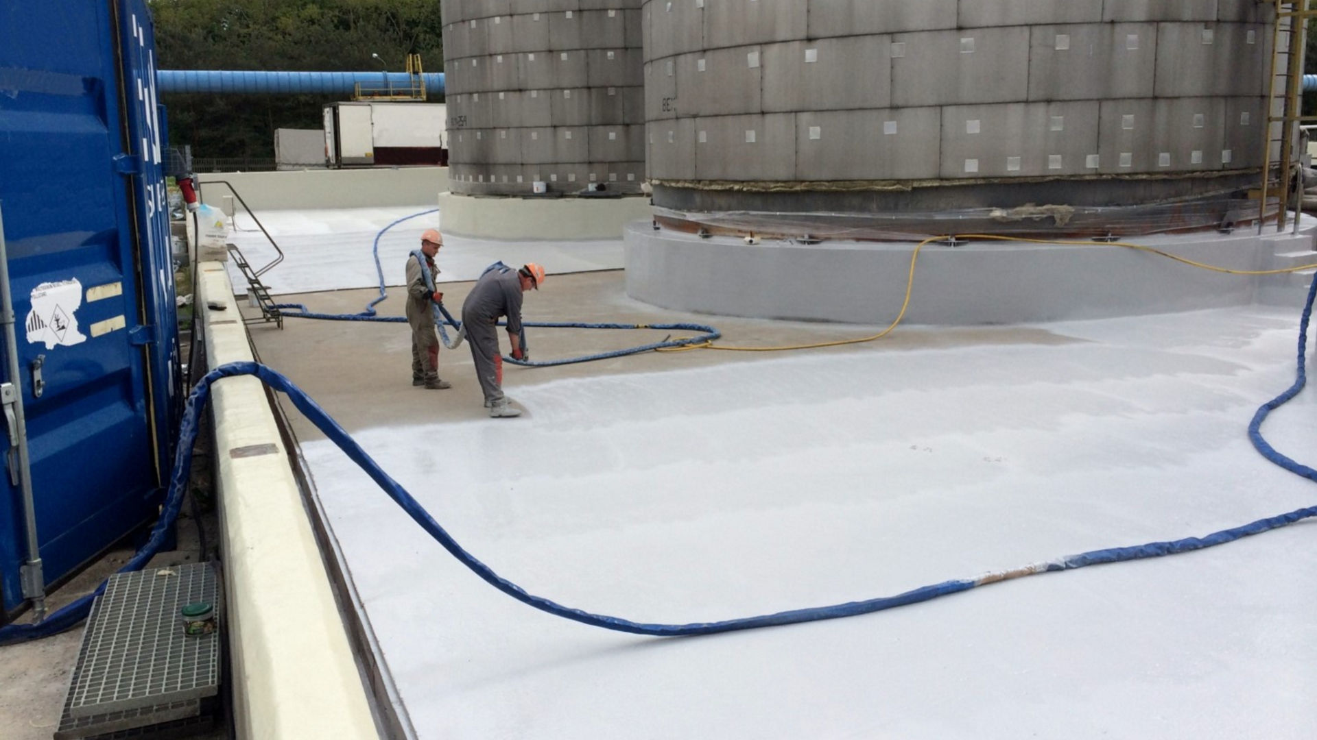 workers applying waterproof coating to tanks