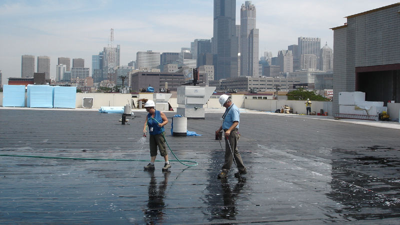 Workers applying sealant on urban rooftop with skyline