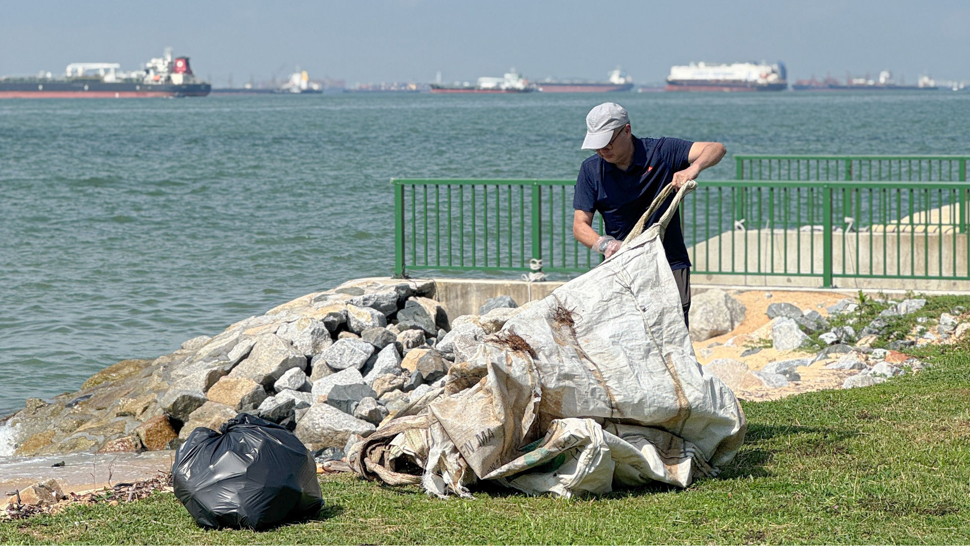 Man cleaning shoreline with ships in background