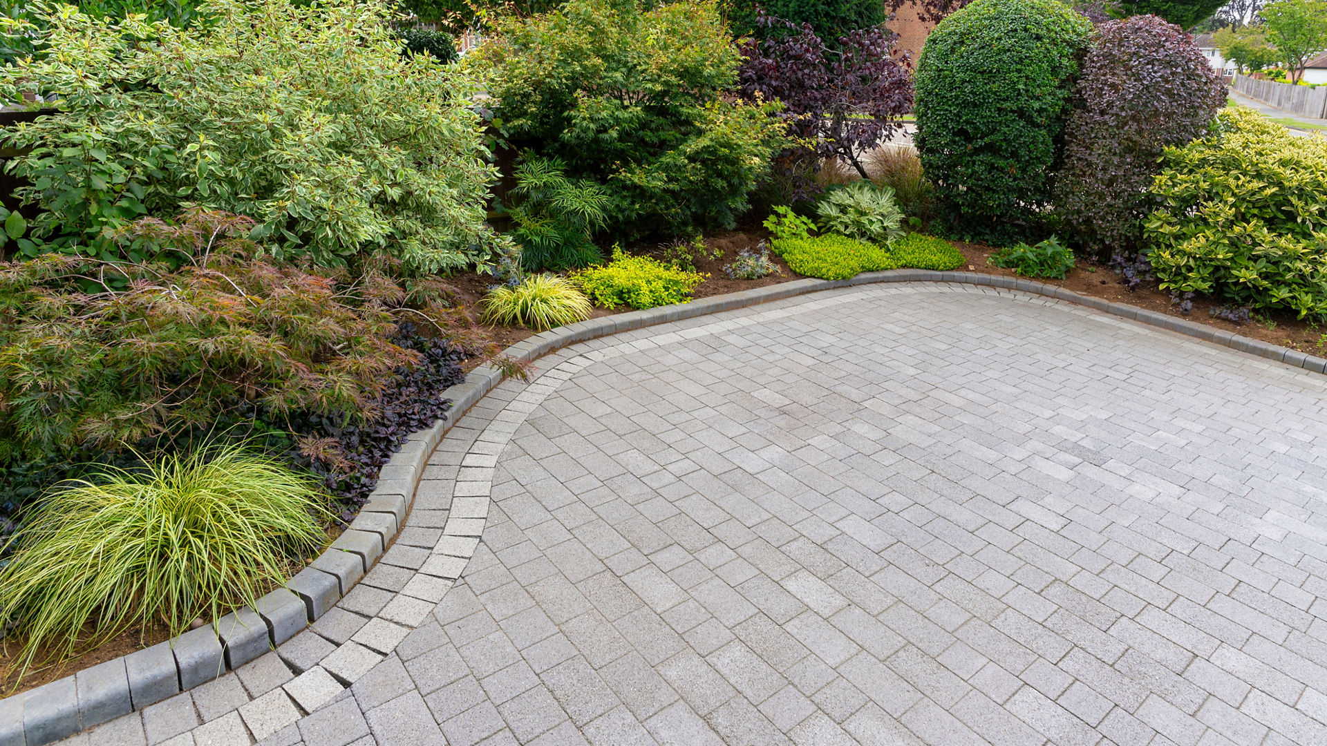 Stylish block paving drive with beautiful garden border with shrubs and flowers