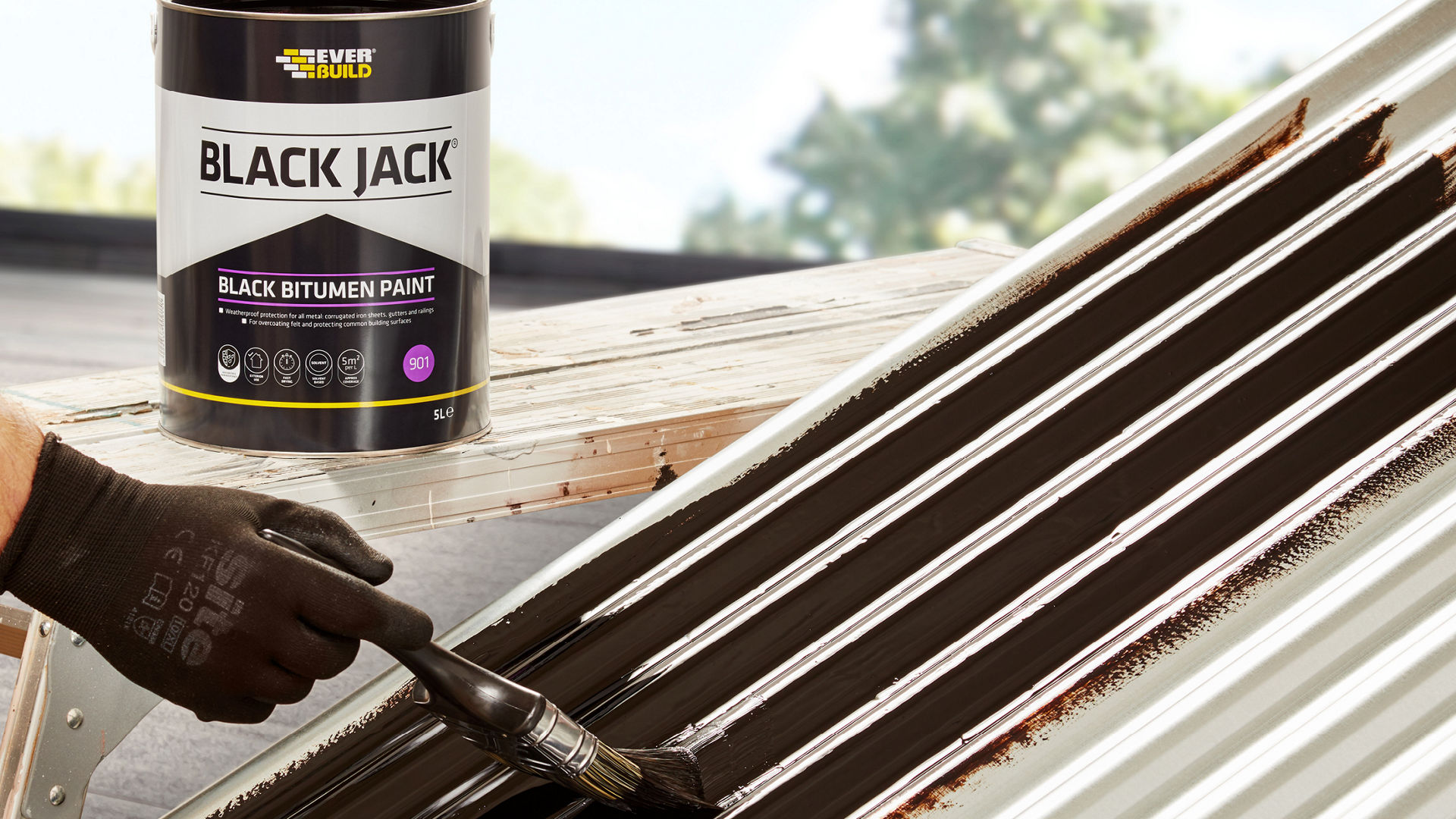 Person applying black bitumen paint to corrugated roof