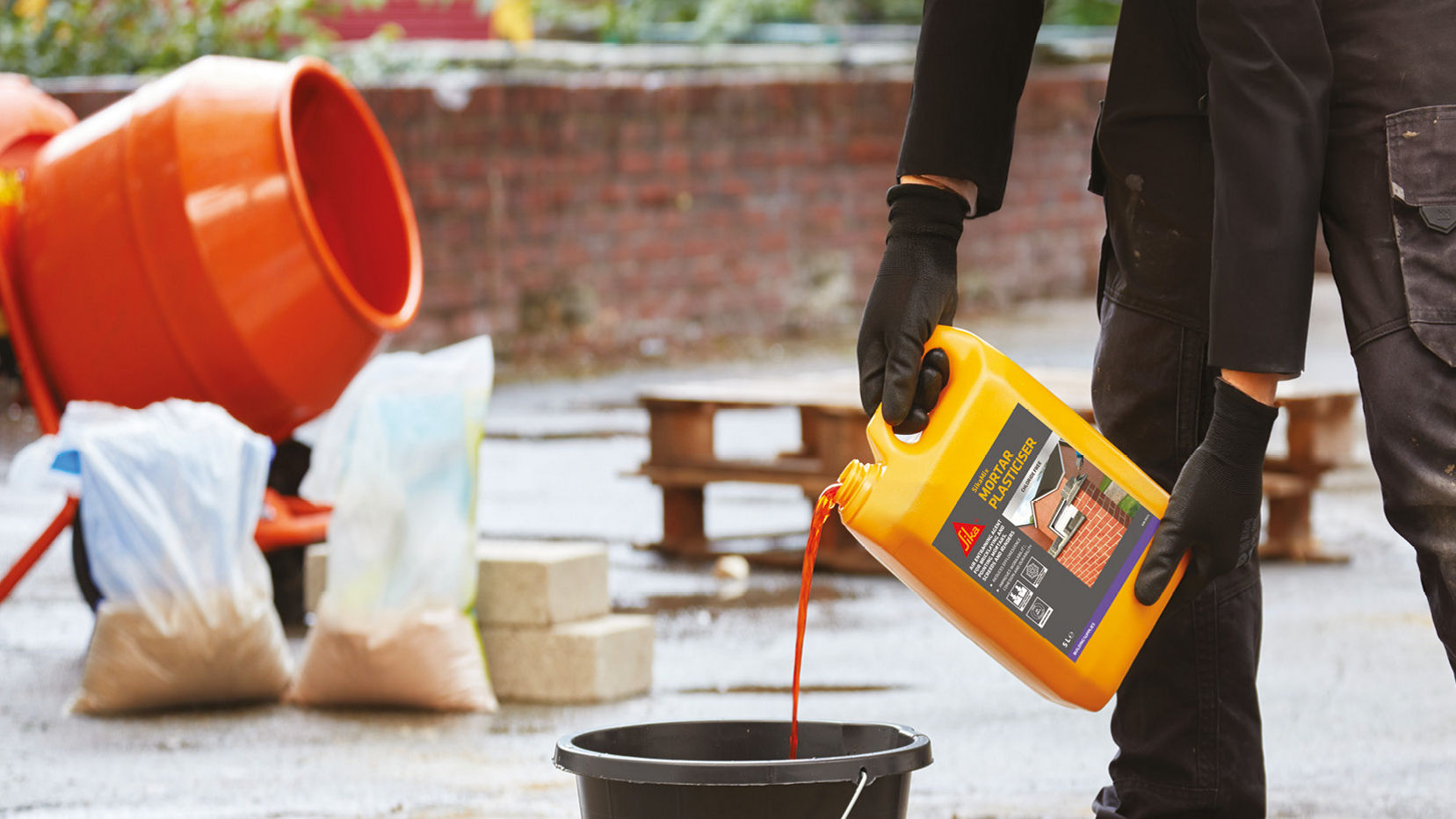 Worker pouring construction liquid into bucket