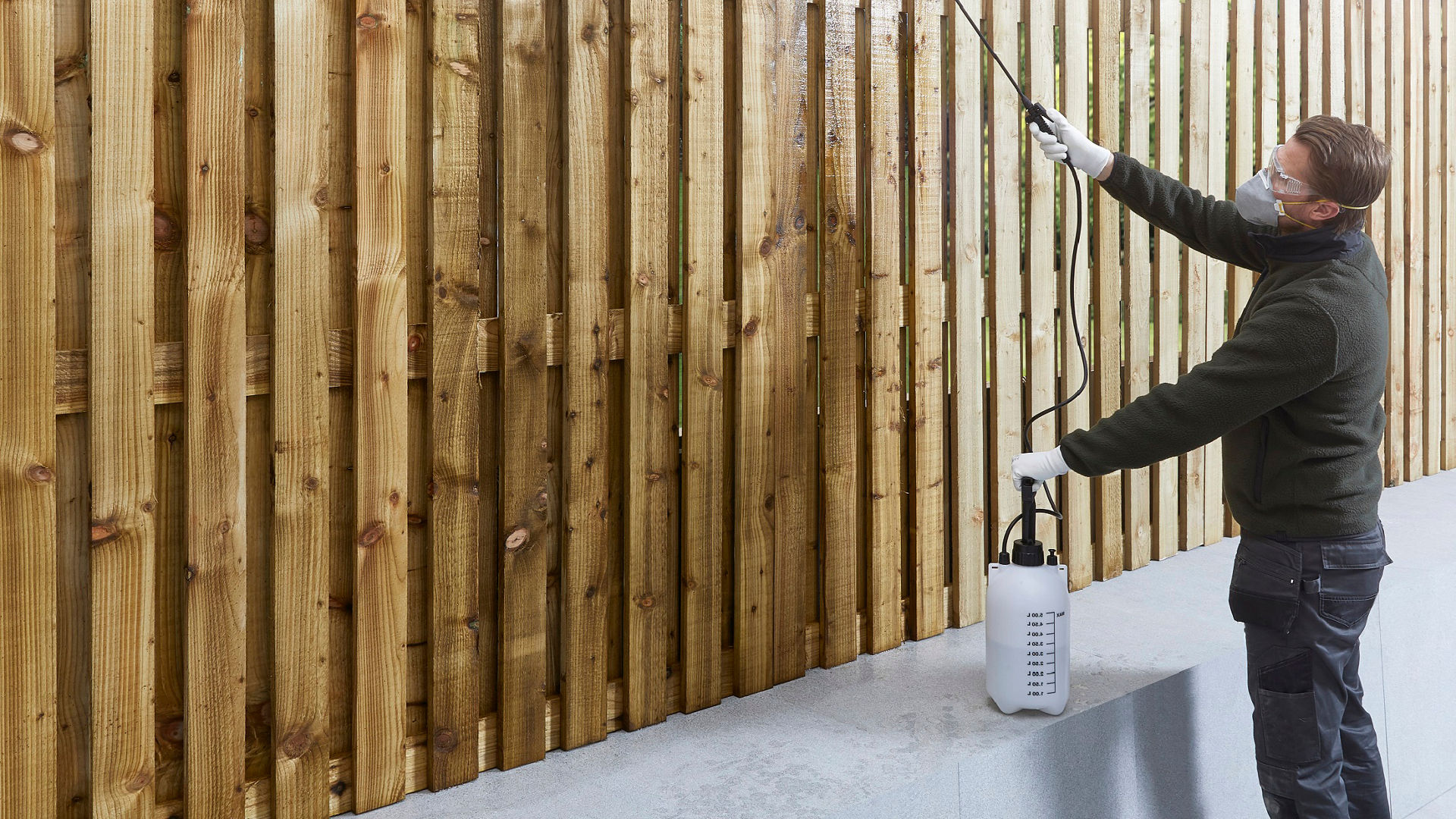 Person spraying wood treatment onto fence