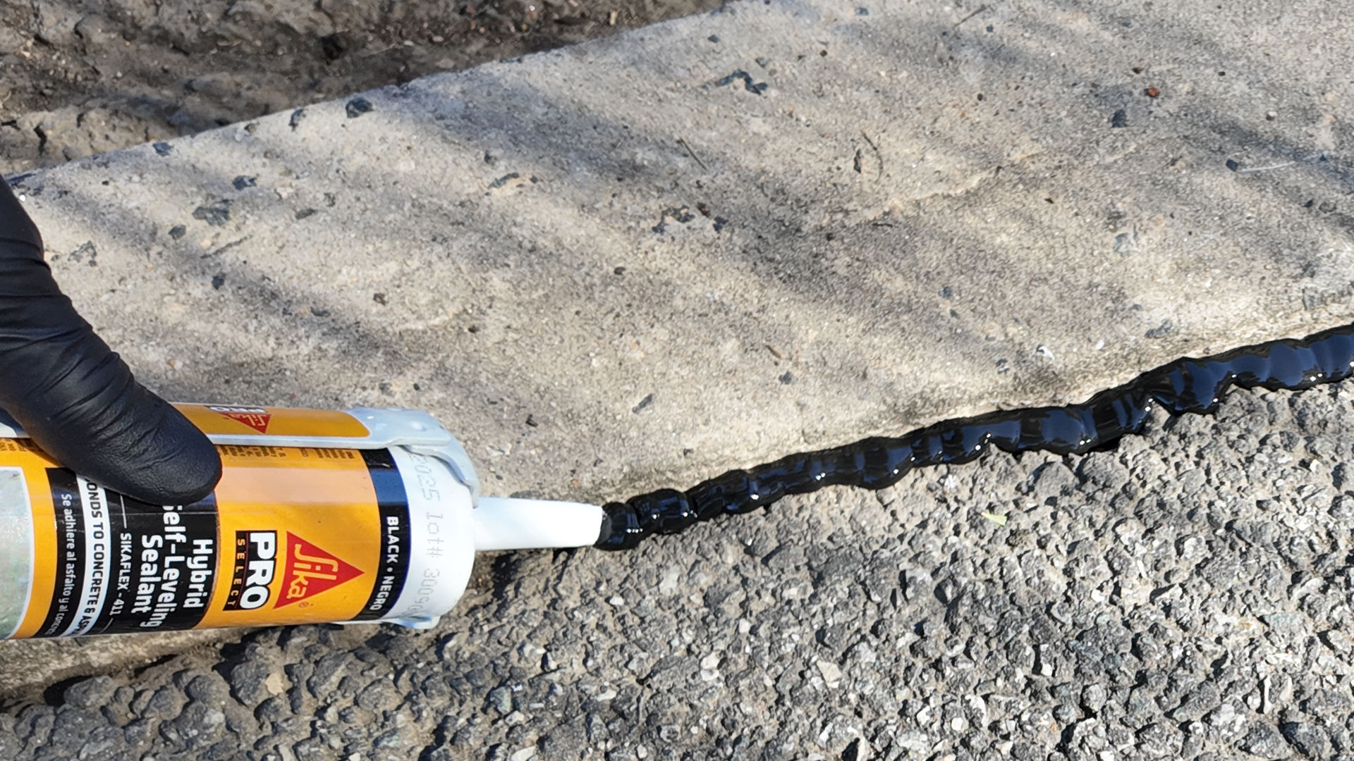 Applying asphalt sealant to concrete crack