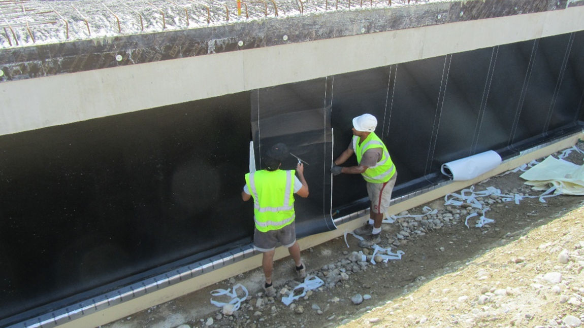 workers in safety vest applying membrane to foundation wall