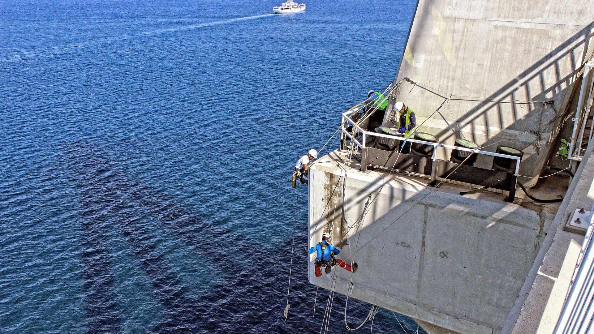   Man repairing a concrete bridge, hanging over the sea	 